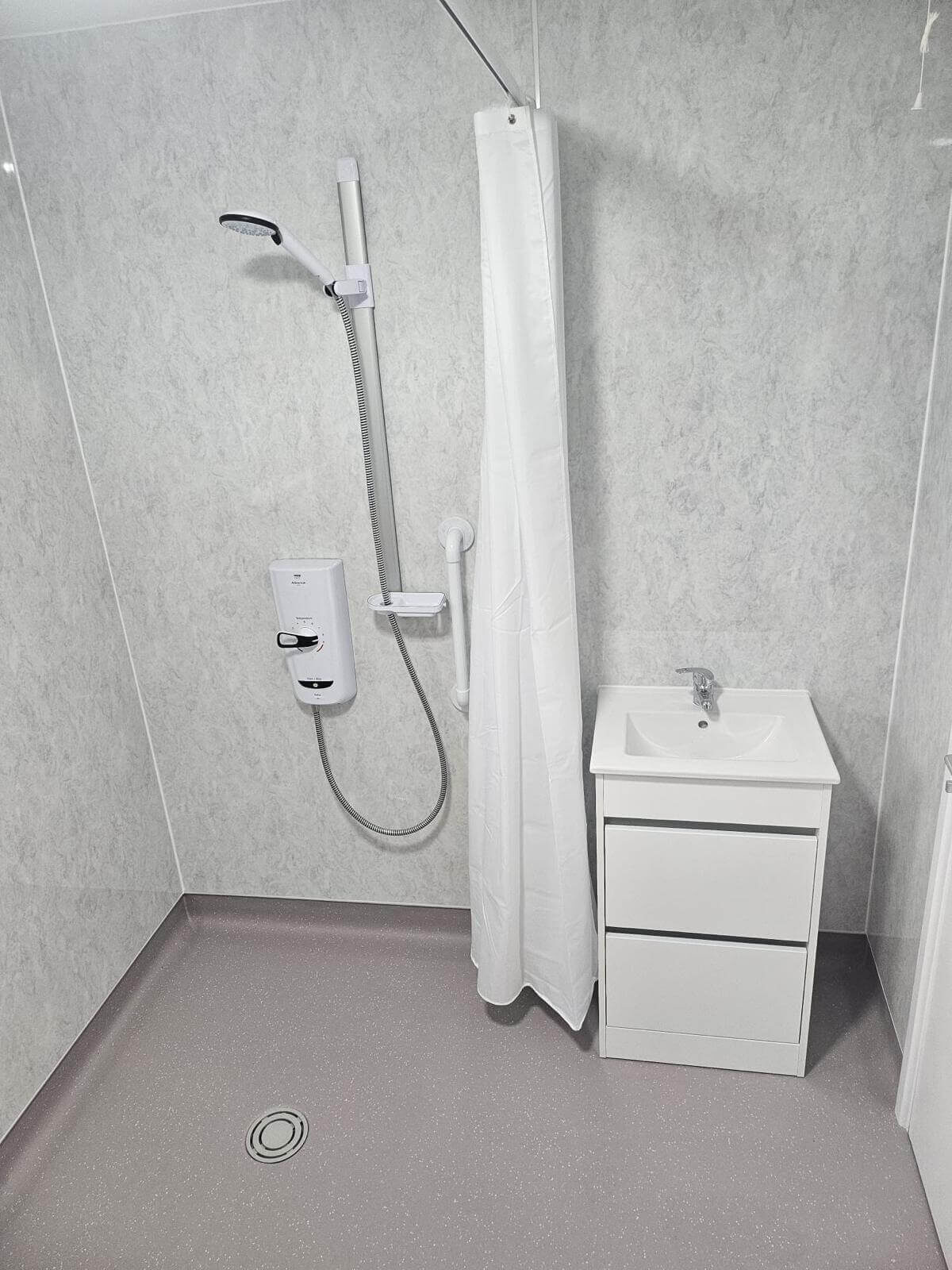 A new wetroom with a shower, shower curtain and sink with storage